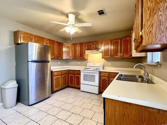 kitchen with under cabinet range hood, freestanding refrigerator, brown cabinetry, electric range, and a sink