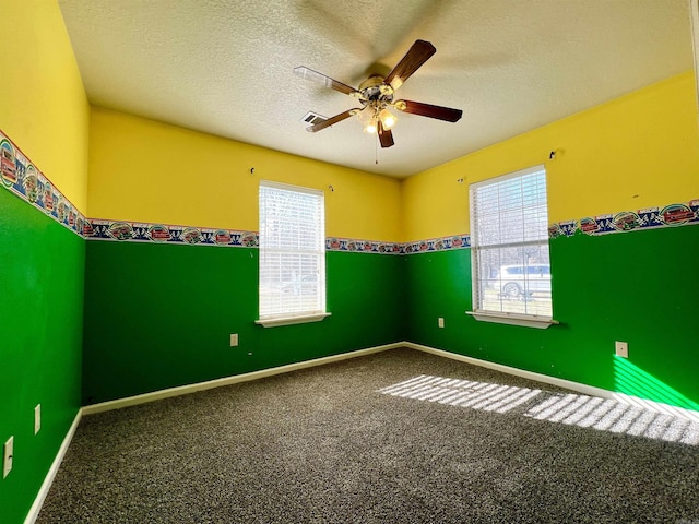 carpeted spare room with plenty of natural light, a ceiling fan, visible vents, and a textured ceiling