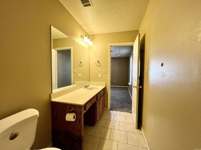 half bathroom with visible vents, toilet, vanity, tile patterned floors, and a textured ceiling