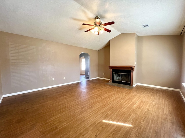 unfurnished living room with a fireplace with flush hearth, a ceiling fan, wood finished floors, arched walkways, and lofted ceiling