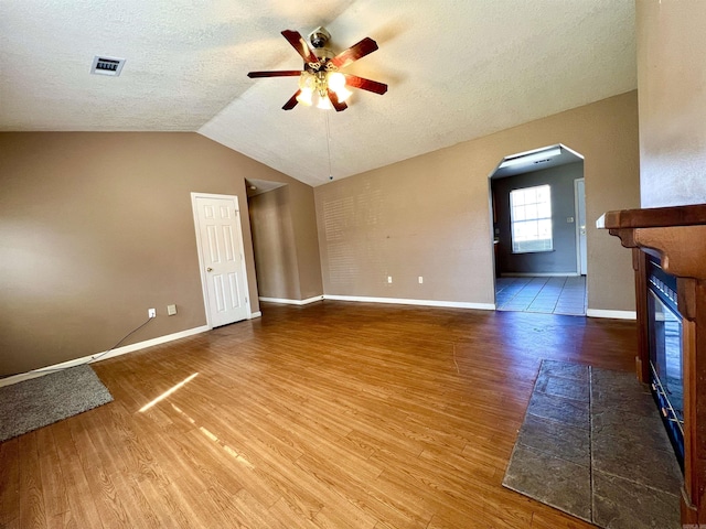 unfurnished living room featuring arched walkways, visible vents, a ceiling fan, and wood finished floors