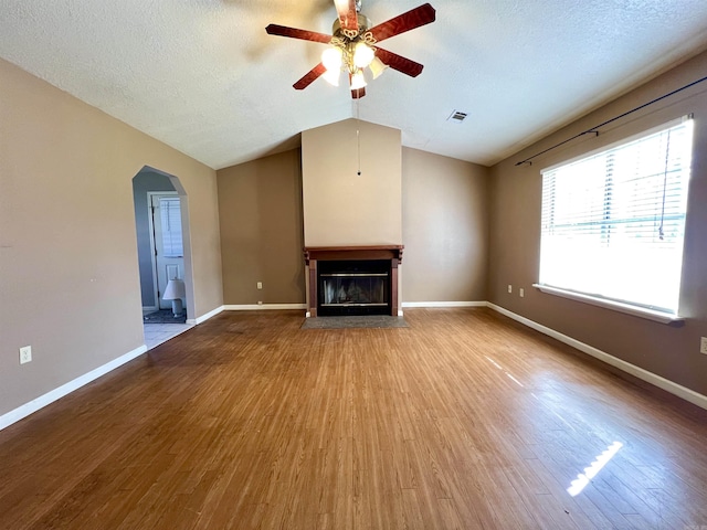 unfurnished living room featuring arched walkways, visible vents, a fireplace with flush hearth, and wood finished floors