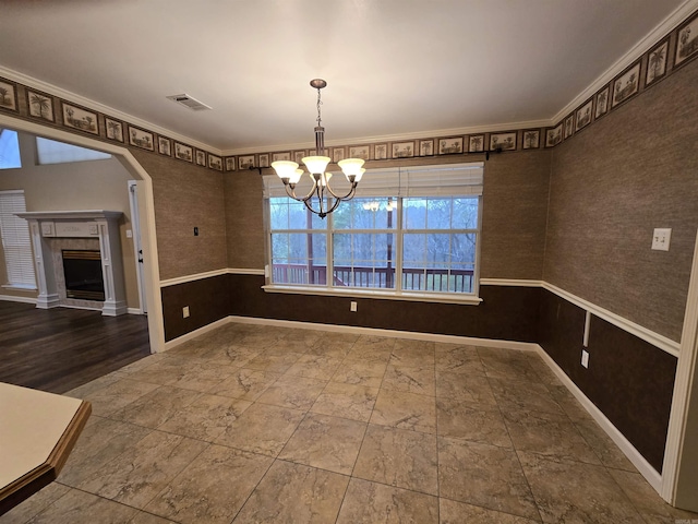 unfurnished dining area with visible vents, baseboards, arched walkways, a tiled fireplace, and a notable chandelier