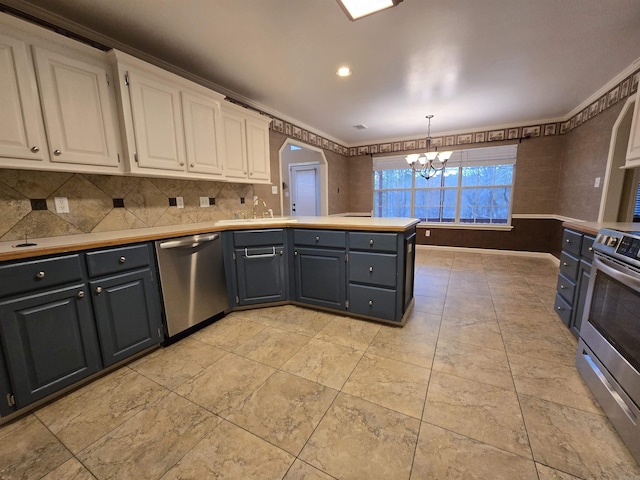 kitchen with a sink, a peninsula, appliances with stainless steel finishes, white cabinets, and a chandelier