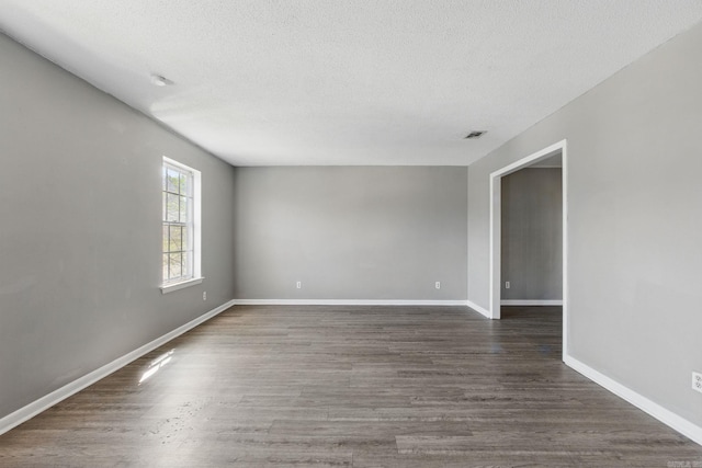 empty room featuring visible vents, baseboards, dark wood-type flooring, and a textured ceiling