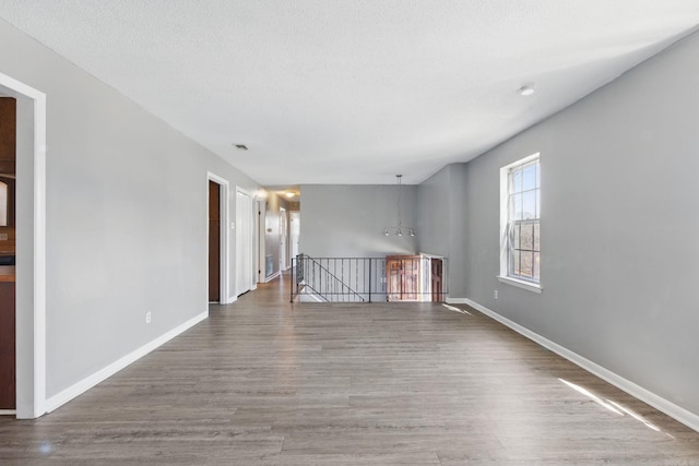 empty room with an inviting chandelier, wood finished floors, baseboards, and a textured ceiling