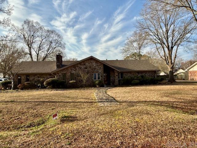 view of front facade featuring a front yard, stone siding, and a chimney