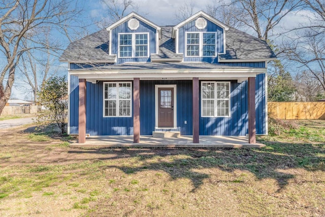 view of front facade with a porch, roof with shingles, board and batten siding, and fence