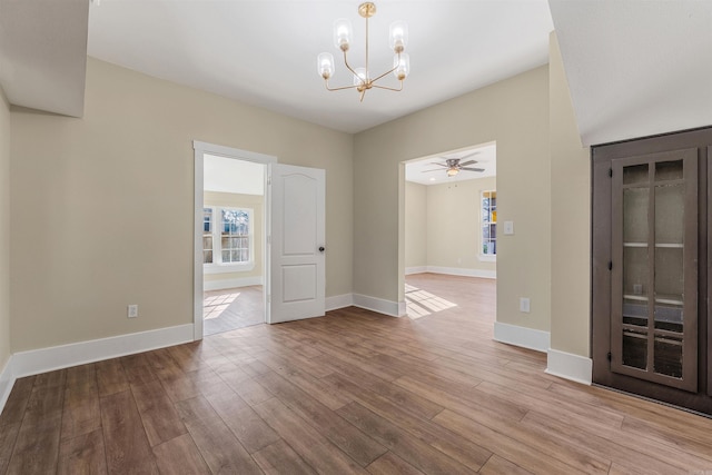 empty room featuring ceiling fan with notable chandelier, wood finished floors, and baseboards