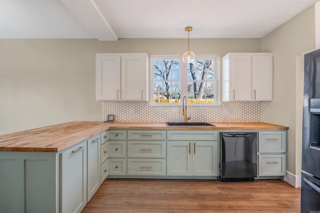 kitchen featuring a sink, wood counters, black dishwasher, a peninsula, and decorative backsplash