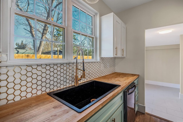 kitchen with white cabinetry, butcher block countertops, decorative backsplash, a sink, and dishwasher