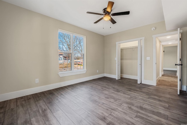 unfurnished bedroom featuring baseboards, dark wood-style flooring, a closet, and ceiling fan