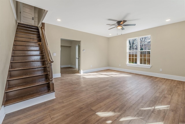 unfurnished living room with stairs, baseboards, wood finished floors, and a ceiling fan