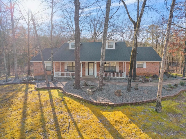 rear view of property with brick siding, covered porch, and roof with shingles