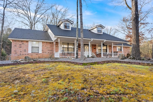 view of front of house featuring brick siding, a porch, a front lawn, and roof with shingles