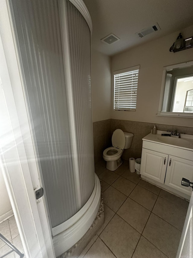 bathroom with tile patterned flooring, visible vents, toilet, and tile walls