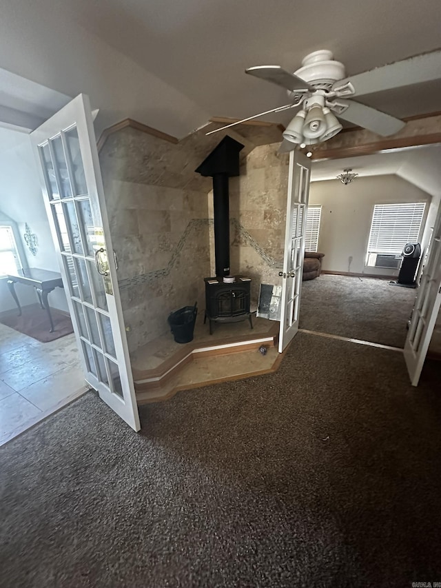 unfurnished living room featuring french doors, carpet, a wood stove, and a ceiling fan