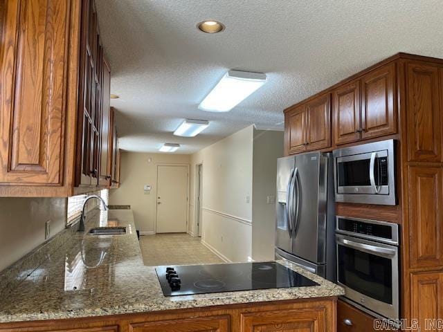 kitchen with a sink, stainless steel appliances, brown cabinets, and stone counters