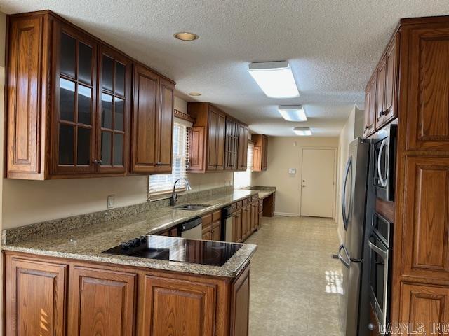 kitchen featuring light stone counters, light floors, a peninsula, glass insert cabinets, and brown cabinets