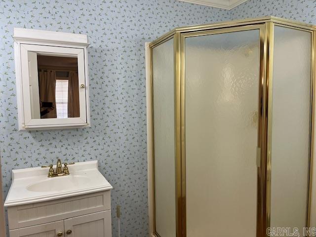 full bathroom with vanity, a shower stall, and wallpapered walls