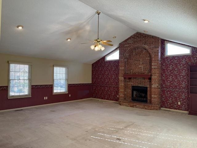 unfurnished living room featuring wallpapered walls, lofted ceiling, a wealth of natural light, and wainscoting