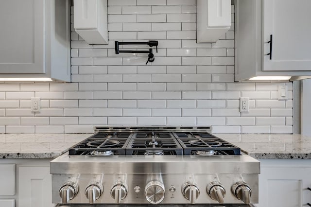 kitchen with white cabinetry, stove, light stone countertops, and backsplash