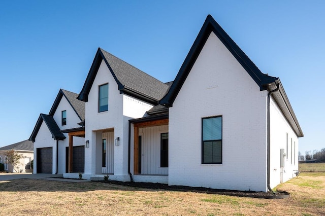 modern farmhouse style home with driveway, a front lawn, a shingled roof, a garage, and brick siding