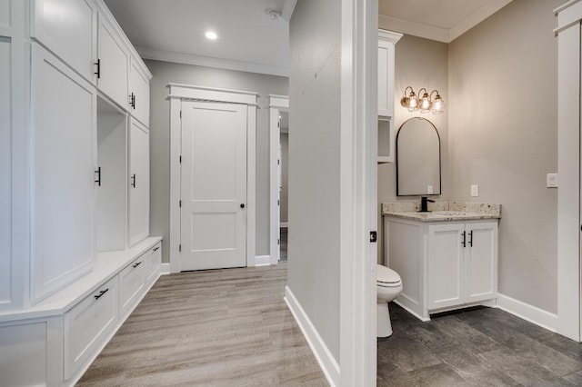 bathroom with toilet, ornamental molding, wood finished floors, baseboards, and vanity