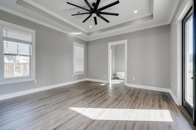 unfurnished bedroom with multiple windows, baseboards, a tray ceiling, and wood finished floors