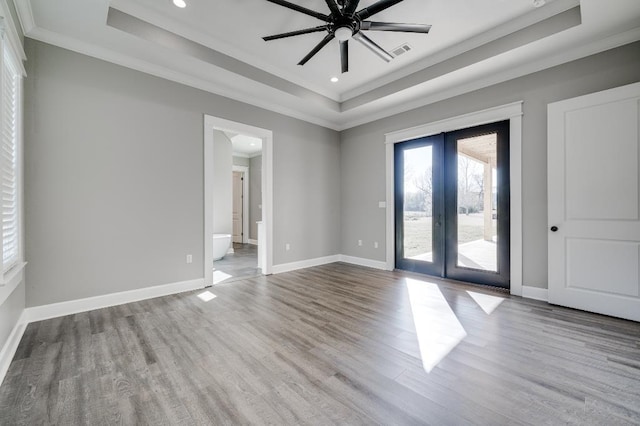 spare room featuring a raised ceiling, wood finished floors, baseboards, and visible vents