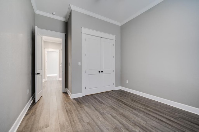 unfurnished bedroom with wood finished floors, baseboards, a closet, and ornamental molding