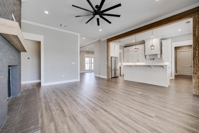 unfurnished living room with light wood finished floors, baseboards, ornamental molding, a fireplace, and a ceiling fan