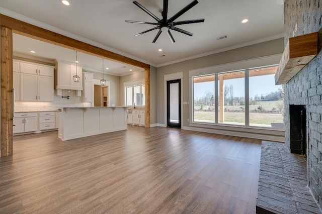 unfurnished living room featuring wood finished floors, a ceiling fan, visible vents, a fireplace, and ornamental molding