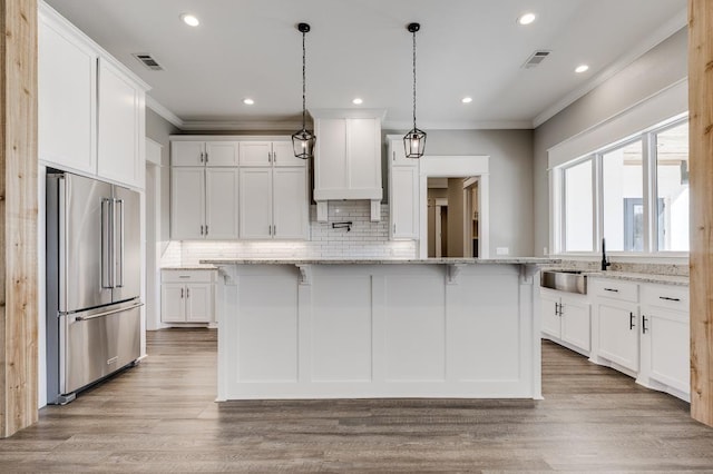 kitchen featuring visible vents, high end fridge, ornamental molding, a sink, and white cabinets