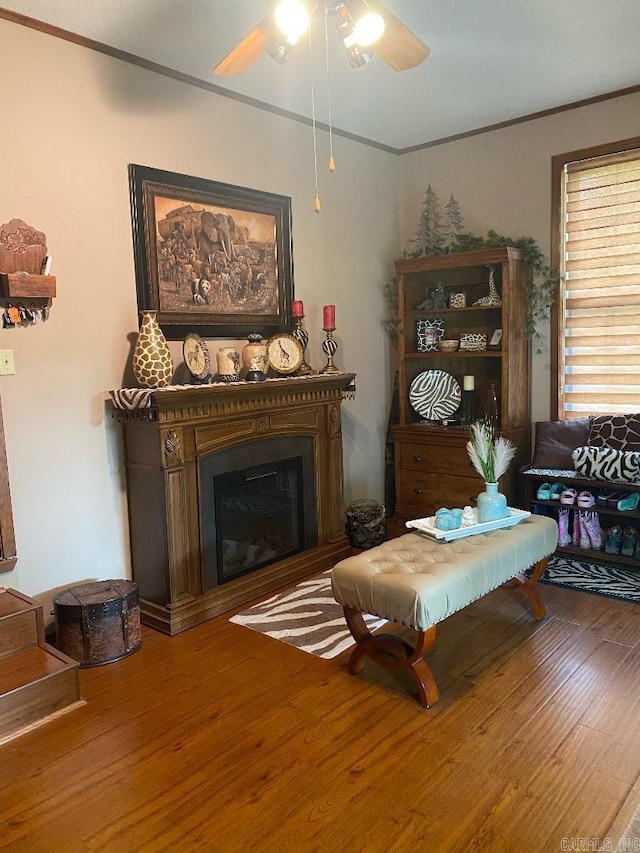 living area featuring a fireplace, crown molding, wood finished floors, and ceiling fan