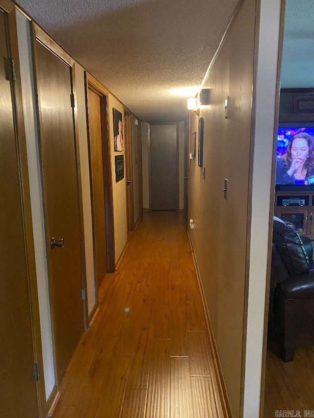 corridor with a textured ceiling, light wood-type flooring, and baseboards