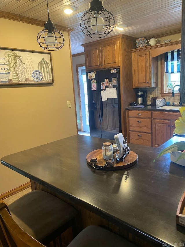 kitchen featuring dark countertops, brown cabinetry, a sink, crown molding, and black fridge