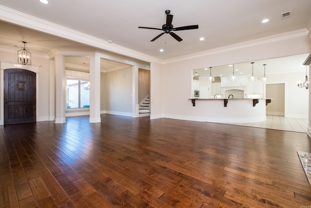 unfurnished living room with ornamental molding, ceiling fan with notable chandelier, stairway, wood-type flooring, and baseboards