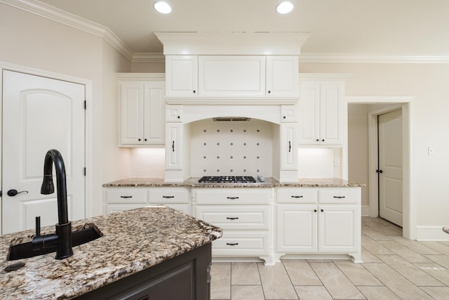 kitchen featuring light stone countertops, stainless steel gas cooktop, decorative backsplash, white cabinetry, and crown molding