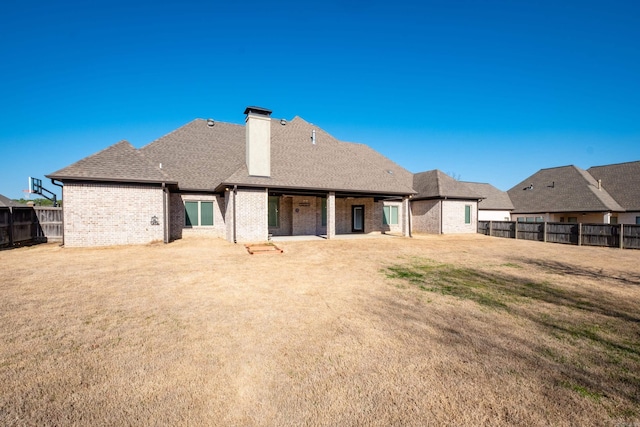 rear view of house with roof with shingles, a yard, a fenced backyard, a chimney, and brick siding