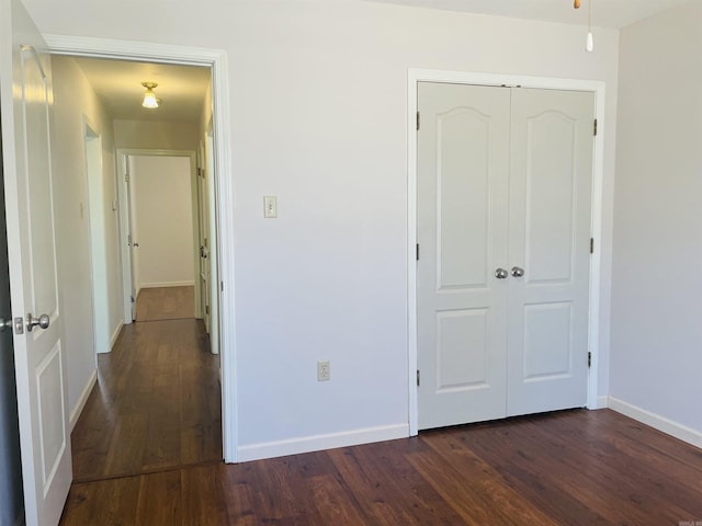 unfurnished bedroom featuring a closet, baseboards, and dark wood-style floors