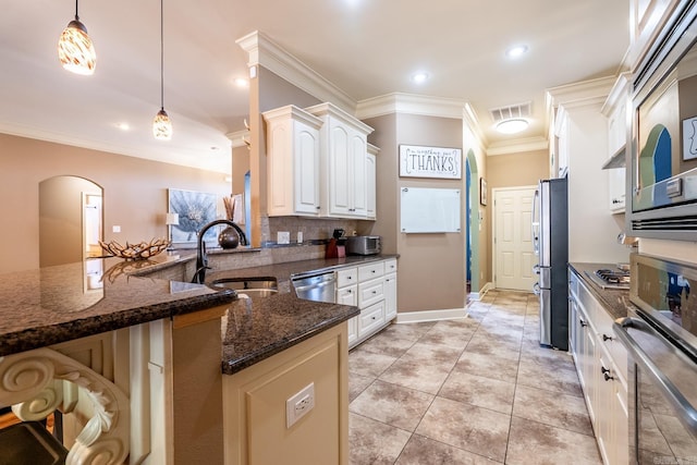 kitchen featuring arched walkways, a sink, stainless steel appliances, pendant lighting, and crown molding