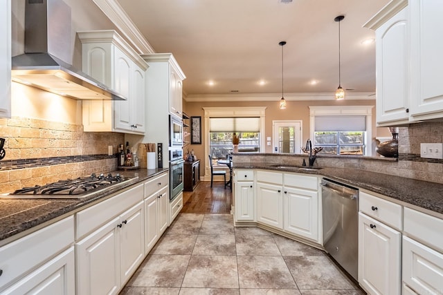 kitchen featuring wall chimney range hood, ornamental molding, appliances with stainless steel finishes, white cabinets, and a sink