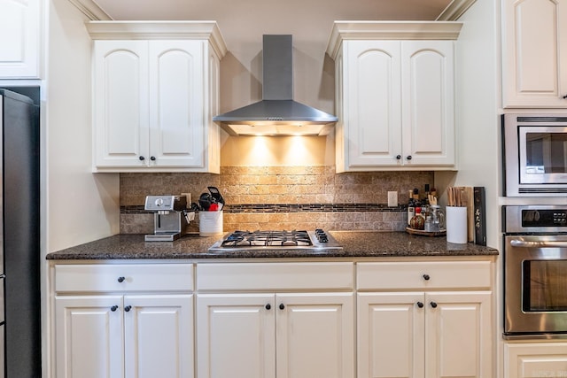 kitchen with dark stone countertops, wall chimney range hood, backsplash, and stainless steel appliances