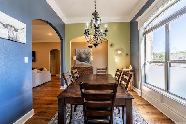 dining space featuring arched walkways, a chandelier, crown molding, and wood finished floors