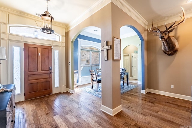 entrance foyer with crown molding, baseboards, a chandelier, wood finished floors, and arched walkways