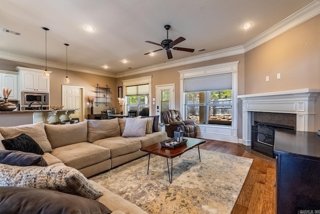 living area with ornamental molding, wood finished floors, visible vents, and ceiling fan