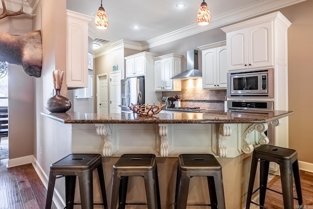 kitchen with ornamental molding, stainless steel appliances, a breakfast bar area, wall chimney exhaust hood, and decorative backsplash