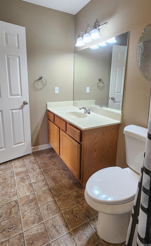 bathroom with vanity, toilet, baseboards, and stone tile flooring