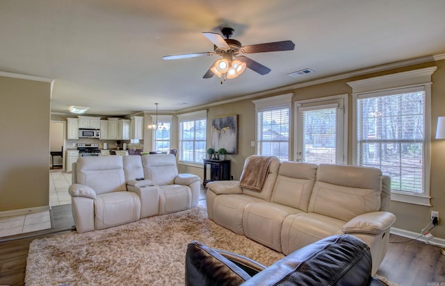 living room with visible vents, light wood-style floors, ornamental molding, and ceiling fan with notable chandelier